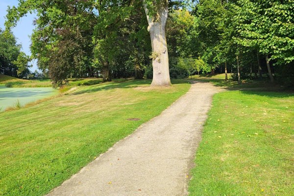 Maak Limburg toegankelijk, met Nobre Cál halfverharding. Een kronkelend pad leidt door een groen park met bomen en een vijver aan de linkerkant.